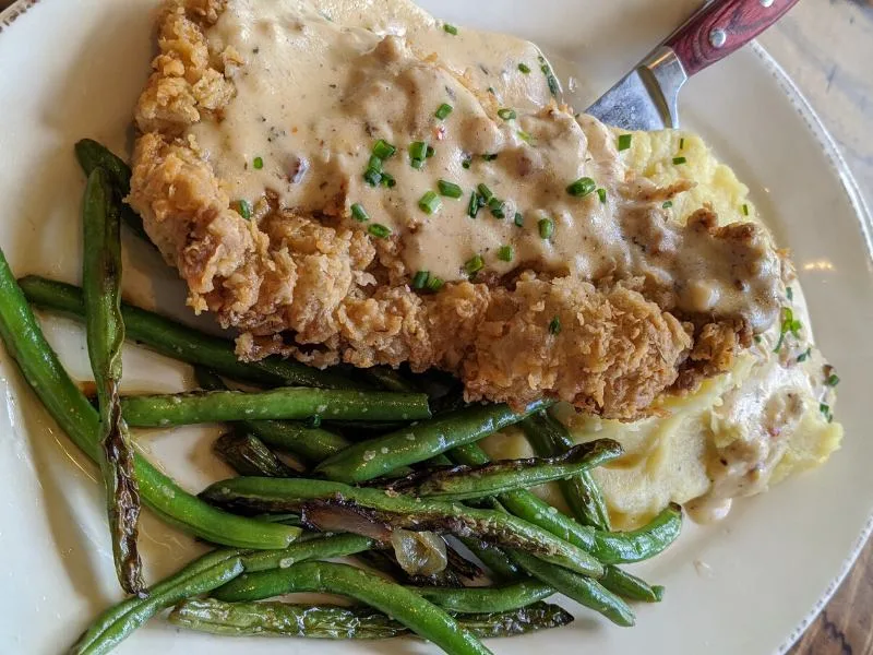 Country fried steak with masked potatoes and green beans on white plate 
