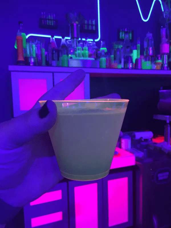 holding a drink in a room with black light 